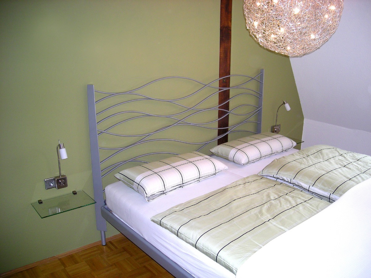 Schlafzimmer-Gestaltung: Ein filigranes Metall-Doppelbett mit seitlich angeordneten Glasboarden als platzsparender Nachttisch-Ersatz